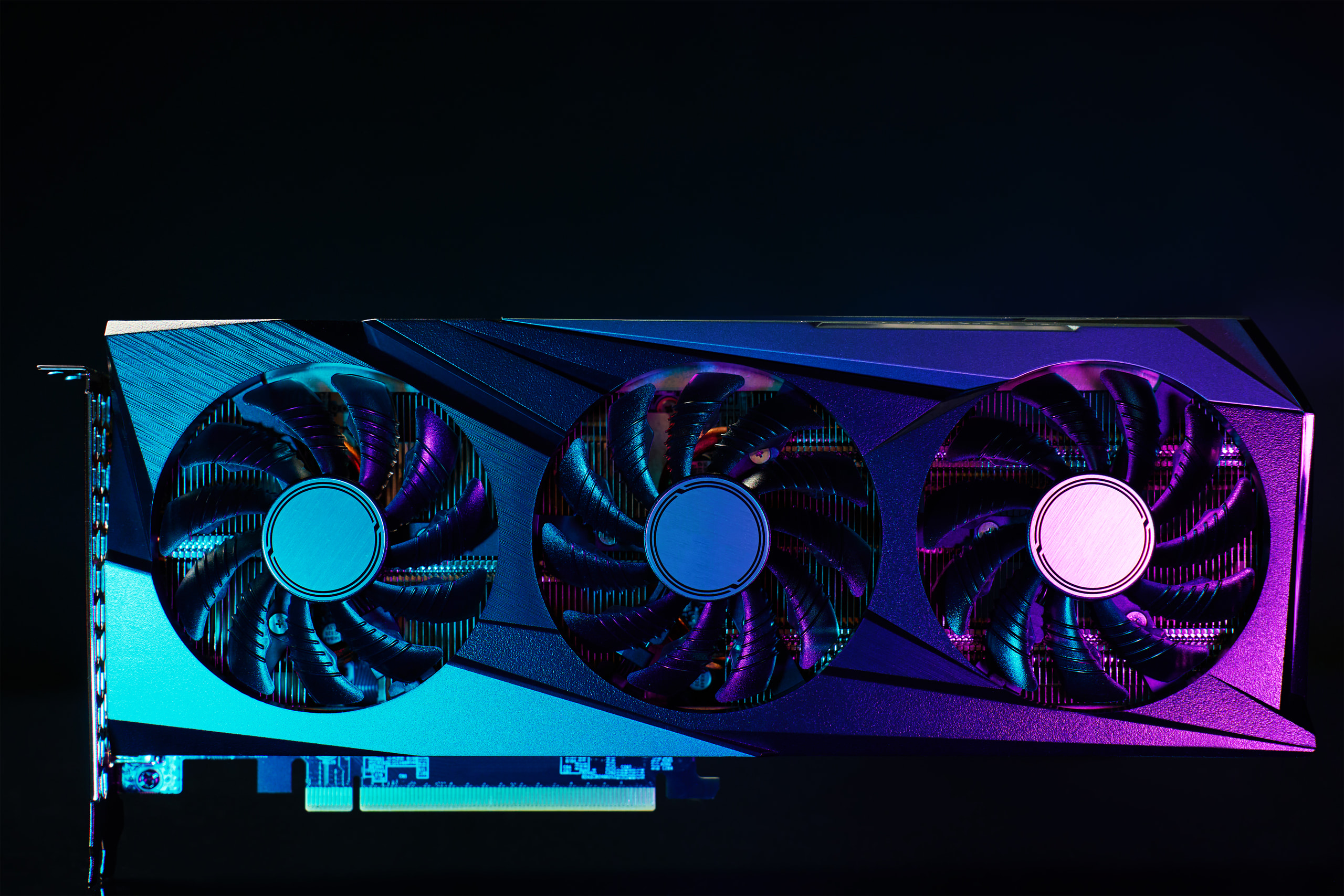 Studio product shot of a triple-fan graphics card under blue and magenta light
